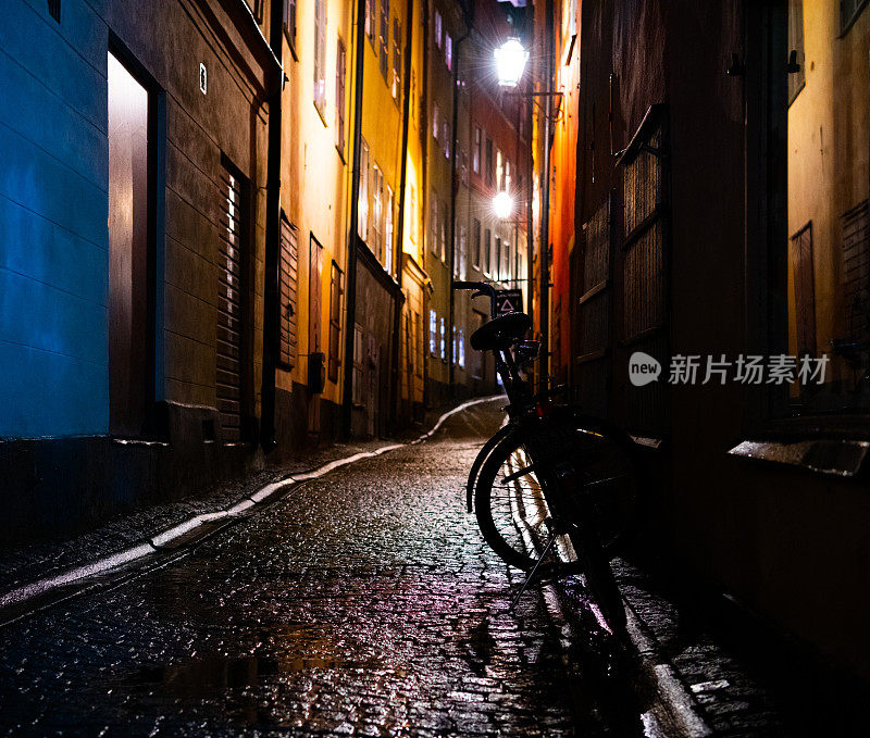 一辆自行车停在斯德哥尔摩老城“Gamla Stan”的一个冬天的晚上。街灯在雨水中反射着潮湿的鹅卵石